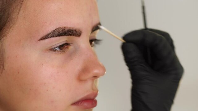 Eyebrow coloring. Professional styling, correction and lamination procedures of female eyebrows in beauty salon. Closeup view 4k video of client face and stylist's hands working in black gloves.