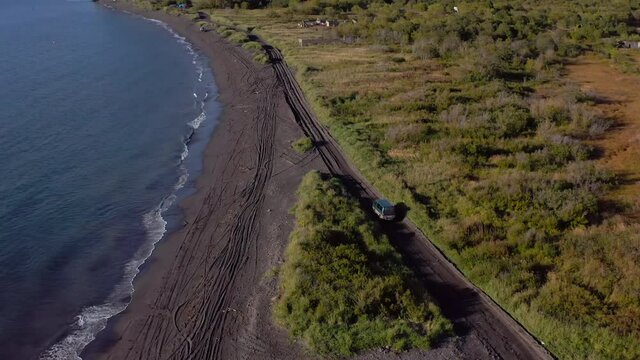 A small van drives on a road with black volcanic pex. The coast of the Avacha Bay. Majestic cliffs, hills and mountains. Seascape. Travel to the Kamchatka Peninsula.