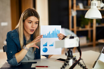 Young business woman recording video for her vlog shows papers with graphs