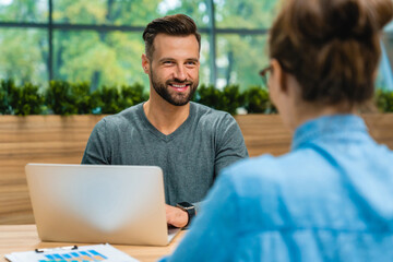 Male worker and customer talking together at office desk using laptop