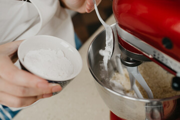 Fototapeta na wymiar A close photo of powdered sugar is falling from the spoon into the stainless steel bowl of the red stand mixer which is mixing shortcrust pastry.