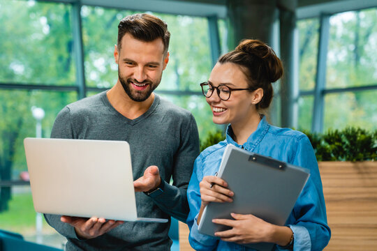 Two smiling caucasian colleagues looking at laptop together during discussion in office