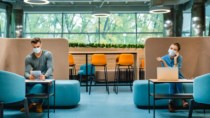 Social distancing concept. Two colleagues sitting in 1.5 metres distance in medical masks against Covid19 in modern office