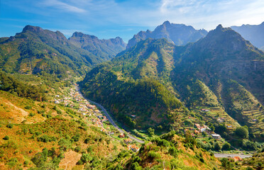 Fototapeta na wymiar Traveling Madeira. View on valley with houses and winding road against steep peaks from Encumeada hiking path. Portugal.