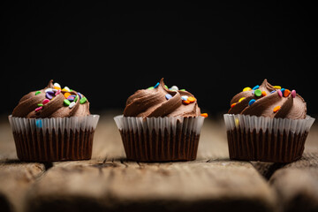 Tasty chocolate cupcakes on rustic wooden table on black background. Sweet dessert. Bakery concept. Elegant food. Sweets for coffee or tea. Space for text.