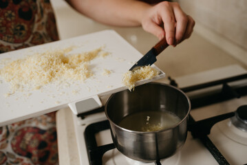 A close photo of a hand of a woman who is throwing lemon zest off the board with a knife to fresh lemon juice in the saucepan on the gas stove