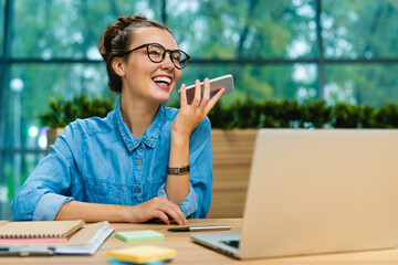 Pretty young business woman recording voice message on her working place in office