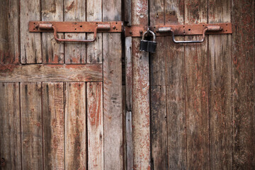 Padlock and rusty metal handles on the gate made of old, textured wood with peeling paint.The texture of a wooden Board. Old board.