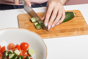 a woman cuts cucumbers into cubes on a salad cutting Board