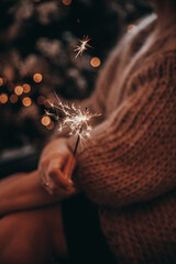 Closeup of a woman holding a sparkler miracle candle in a cozy winter sweater. Bokeh Christmas...