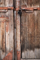 The gate is made of an old, textured Board with peeling paint, rusty metal handles and a barn padlock. Texture of old wood.