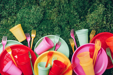 Colored plastic disposable tableware on green grass moss background. Top view. Copy space. Birthday...