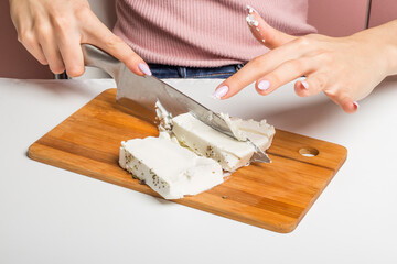 a woman cuts feta cheese into cubes on a cutting Board