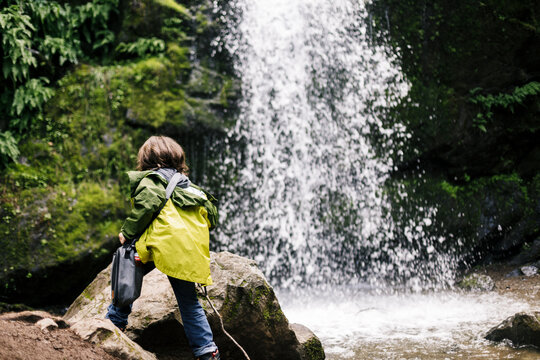 Back view child climbing and holding bag by waterfall