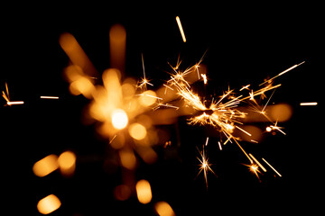 Burning sparkler and spots of light against black background