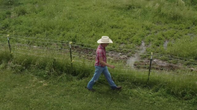 Cowboy rancher walking along a fence and muddy ground