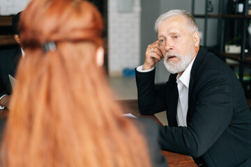 Skilled mature adult male businessman having meeting with young diverse multi-ethnic business colleagues in modern office. Multiethnic business team of businessmen people discussing new project.