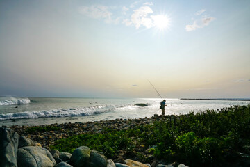 Fisherman walking on ocean beach at sunset.