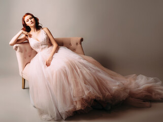 Beautiful bride in a pink wedding dress sitting in a vintage sofa. Studio portrait on neutral...