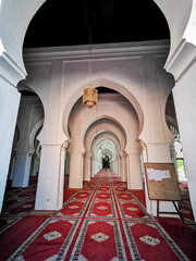 The interior Islamic beauty of the Koutoubia mosque in Marrakesh. The mosque has red Moroccan carpets laid down on the ground with white arches and a long hallway