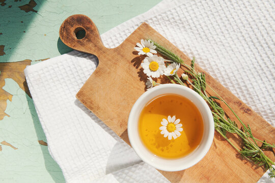 Cup of chamomile tea with chamomile flower, bouquet on cutting board and white towel . Doctor treatment, immune concept, traditional medicine.