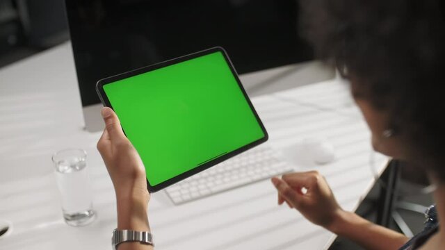View From the Shoulder of Man Using Hand Gestures Swipe Up on Green Mock-up Screen Digital Tablet Computer in Landscape Mode Sitting at The Desk in The Office.
