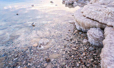 Sand and stones covered with crystalline salt on shore of Dead Sea, clear water near - typical scenery at Ein Bokek beach, Israel