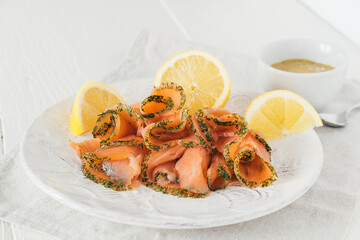 Smoked salmon rolls with lemon on white plate and mustard dip in white bowl on white wooden background