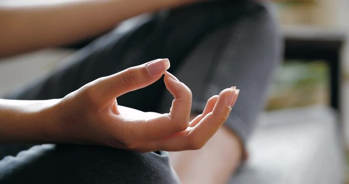 Woman wearing casual jeans clothes sitting on sofa in room in lotus position with crossed legs, doing yoga home, practicing asanas, gaining energy, relaxing, concentrate zen harmony concept, close up