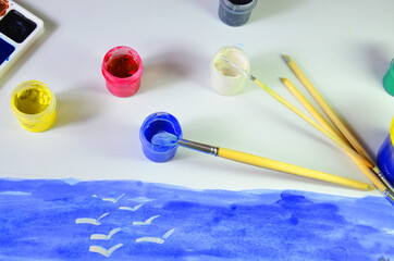 gouache paint brushes and children's drawings. photo child paints a brush with watercolor honey paints. children's art, painting, earlier development watercolor paint blue yellow