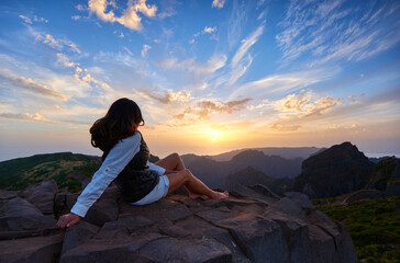 Holidays in Madeira. Middle aged woman with long hair wearing a white sport dress watches sunset over mountainscape of Madeira from highest point of Pico do Arieiro mountains peak.