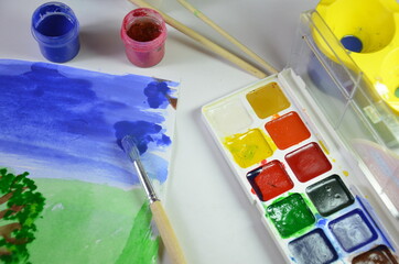 gouache paint brushes and children's drawings. photo child paints a brush with watercolor honey...