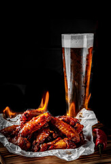 glass of fresh beer and fried chicken wings on wooden table on black background