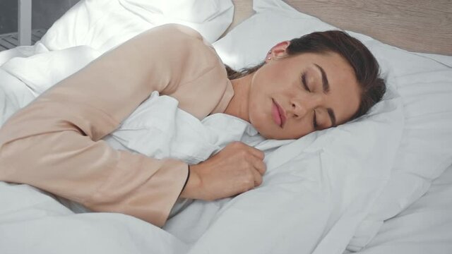 brunette woman sleeping on white bedding in morning