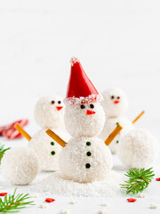 Coconut balls Snowman in santa hat. Funny creative idea for new year and christmas cooking. White background, fir branches, copy space. Festive food, healthy vegan dessert. Homemade Raffaello candies.