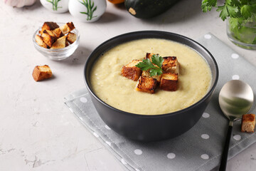 Creamy chicken and zucchini thick soup served with white bread croutons in dark bowl on gray background. Close-up
