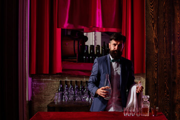 Naklejka premium Waiter bartender. Handsome bearded barman leaning on bar counter. Expert bar man is making cocktail at night club.