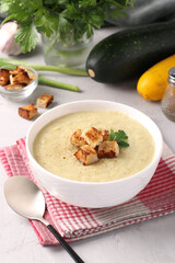 Creamy chicken and zucchini soup served with white bread croutons in a bowl on a gray background.