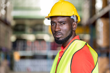 Fototapeta premium Close up of African American male warehouse worker in safety vest and helmet working in in industry storage warehouse with shelf pallet product or spare parts parcel blur background