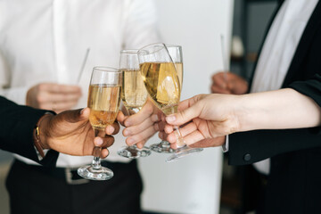 Close-up view of business team of multinational employees holding clinking glasses of champagne and smiling cheerfully at corporate New Year or Happy Christmas eve.