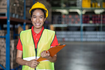 Portrait of African American smiling female warehouse worker with clipboard working and checking products or parcel goods on shelf pallet in industrial storage warehouse