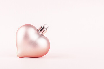 Christmas tree toy in the shape of a heart on a pale pink background with copy space. Close up.