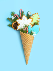 Gingerbread cookies in a waffle cone on a blue background. Spruce twigs and snowflakes.