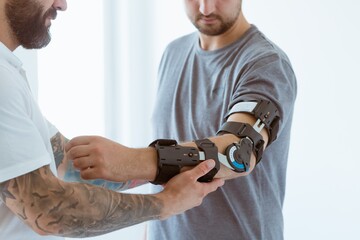 Tattooed physiotherapist who puts an orthosis on the hand of a young patient after an accident