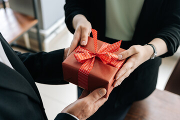 Close-up view of hands of unrecognizable woman giving red gift box tied to bow handed to man....