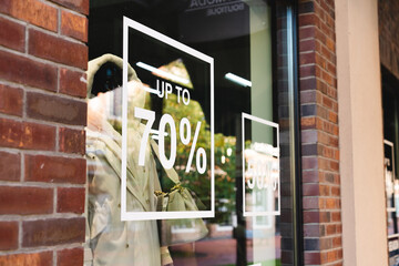Mannequins stand near "70%" discount. Standing in autumn, spring or winter casual clothes. Shop window.