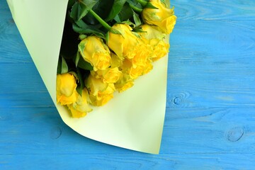 Beautiful Bouquet of fresh yellow roses on blue wooden background with empty space, selective focus. Bunch of yellow flowers. Birthday or holiday bouquet