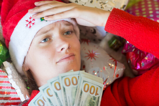 Stressed Woman Holding Many USD Bills By Lots Of Christmas Gifts.