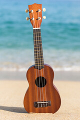 Hawaiian ukulele guitar on the beach sand near the ocean shore.
