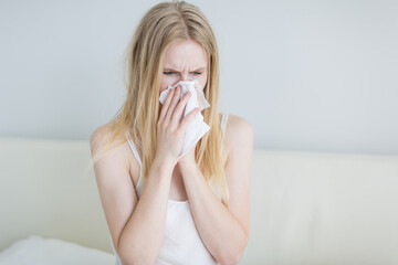 Sick woman blowing her runny nose into a tissue paper at home.